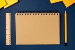 vista superior cuaderno marrón con lápiz amarillo y bloc de notas en la mesa de trabajo azul marino foto