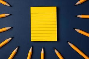 blank yellow sticky note and pencil on navy blue table background photo