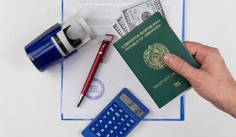 la mano sostiene el pasaporte de uzbekistán con dólares estadounidenses en el fondo de los documentos y el sello de goma. concepto - soborno y corrupción foto
