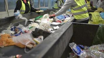 arbeidershanden die plastic afval sorteren dat zich op transportband, afvalsorteerstation beweegt; video