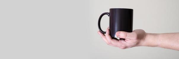 Black mug in the hands of a man on a light background. photo