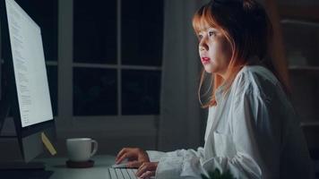 Young asian woman working late using desktop on desk in living room at home. Asia business woman writing notebook document finance and calculator in night at home office. Overworked female concept. photo