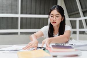 Asian student women reading books in library at university. Young undergraduate girl do homework, read textbook, study hard for knowledge and education on lecture desk at college campus. photo