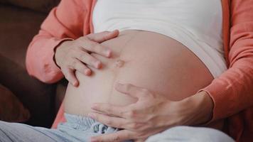 Young Asian Pregnant woman holding her belly talking with her child. Mom feeling happy smiling positive and peaceful while take care baby, pregnancy lying on sofa in living room at home concept. photo