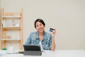 Beautiful smart business Asian woman using tablet buying online shopping by credit card while wear smart casual sitting on desk in living room at home. Lifestyle woman working at home concept. photo