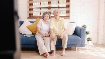 Asian elderly couple watching television in living room at home, sweet couple enjoy love moment while lying on the sofa when relaxed at home. Enjoying time lifestyle senior family at home concept. photo