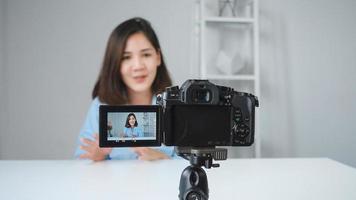 Happy smiling asian woman or beauty blogger with brush and camera recording video and waving hand at home. Beauty videoblog blogging people concept. Dolly shot. photo