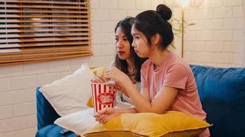 Lesbian lgbt women couple watching movie at home, Asian female lover eating popcorn scary and shock while looking horror film together on sofa in living room in night concept. photo