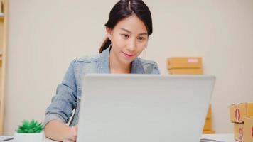 Beautiful smart Asian young entrepreneur business woman owner of SME online checking product on stock and save to computer working at home. Small business owner at home office concept. photo