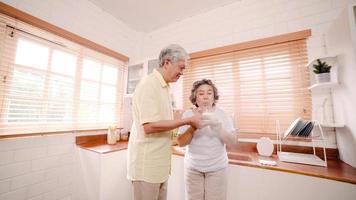 Asian elderly couple man holding cake celebrating wife's birthday in kitchen at home. Chinese couple enjoy love moment together at home. Lifestyle senior family at home concept. photo