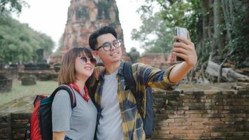 Traveler Asian couple using smartphone taking selfie while spending holiday trip at Ayutthaya, Thailand, Couple enjoy their journey at amazing landmark in traditional city. photo