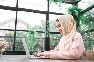 Beautiful young smiling asian muslim woman working on laptop sitting in living room at home. Asian business woman working document finance and calculator in her home office. Enjoying time at home. photo