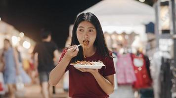 Asian young woman travel in Bangkok, Thailand, beautiful female feeling happy walking and eating Pad Thai at The Khao San Road. Women travel eat street food in Thailand concept. photo