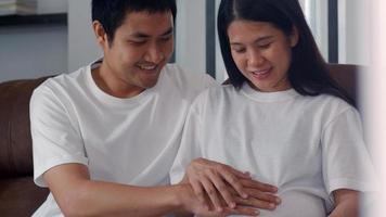 Young Asian Pregnant couple man touch his wife belly talking with his child. Mom and Dad feeling happy smiling peaceful while take care baby, pregnancy lying on sofa in living room at home concept. photo