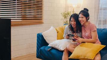 Lesbian lgbt women couple play games at home, Asian female using joystick having funny happy moment together on sofa in living room in night. Young lover football fan, celebrate holiday concept. photo