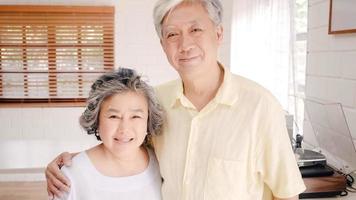 pareja asiática de ancianos que se siente feliz sonriendo y mirando a la cámara mientras se relaja en la sala de estar en casa. Disfrutando del concepto de familia mayor en el hogar del estilo de vida del tiempo. retrato mirando a la cámara. foto