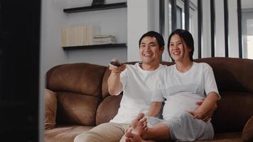 Young Asian Pregnant couple watching TV. Mom and Dad feeling happy smiling peaceful while take care baby, pregnancy lying on sofa in living room at home concept. photo