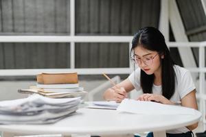 mujeres estudiantes asiáticas leyendo libros en la biblioteca de la universidad. la joven estudiante hace la tarea, lee libros de texto, estudia mucho para obtener conocimiento y educación en el escritorio de conferencias en el campus universitario. foto