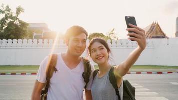 Asian blogger couple travel in Bangkok, Thailand, sweet couple using mobile phone selfie and photo view while spending sweet time in holiday trip in sunset. Couple travel in city concept.