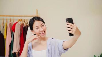 Happy beautiful young Asian woman using smartphone selfie live streaming online to social network. Beauty blogger present beauty cosmetics sitting in front tablet camera for recording video. photo