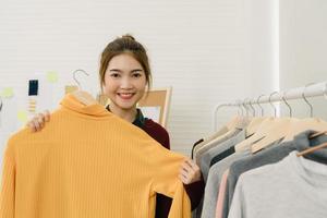 Asian female fashion designer working, checking and choosing clothes design on clothes rack while working in the fashion studio. Lifestyle beautiful professional designer women working concept. photo