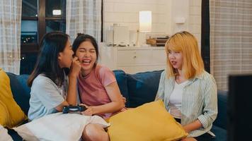 Group of Asian women couple play games at home, female using joystick having funny moment together on sofa in living room in night. Teenager young friend football fan, celebrate holiday concept. photo