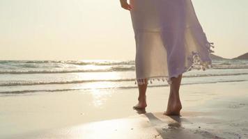 joven mujer asiática caminando en la playa. hermosa mujer feliz relajarse caminando en la playa cerca del mar al atardecer en la noche. las mujeres de estilo de vida viajan en concepto de playa. foto