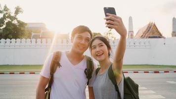 Asian blogger couple travel in Bangkok, Thailand, sweet couple using mobile phone selfie and photo view while spending sweet time in holiday trip in sunset. Couple travel in city concept.