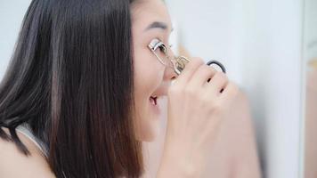 hermosa mujer asiática usando maquillaje rizador de pestañas en el espejo frontal, mujer feliz usando cosméticos de belleza para mejorar lista para trabajar en el dormitorio en casa. las mujeres de estilo de vida se relajan en el concepto de hogar. foto