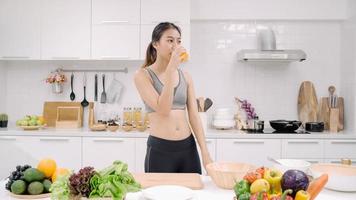 Young Asian woman drinking orange juice in the kitchen, beautiful female in sport clothing use organic fruits lots of nutrition making orange juice by herself at home. Healthy food concept. photo