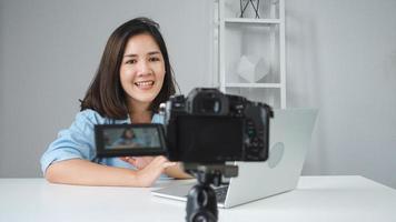 Happy beautiful Asian woman answer question from her subscribers. Female blogger recording video with laptop from camera to filming a question and answer video. photo