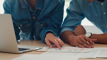 reunión del equipo creativo asiático joven que trabaja en la computadora portátil. grupo de hombres y mujeres de negocios que buscan papel de documento, discuten y piensan en nuevas ideas, situación de negocios, trabajo en equipo en el concepto de oficina moderna. foto