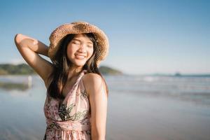 Young Asian woman feeling happy on beach, beautiful female happy relax smiling fun on beach near sea when sunset in evening. Lifestyle women travel on beach concept. photo