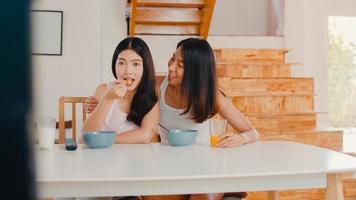 Asian Lesbian lgbtq women couple have breakfast at home, Young Asia lover girls happy watching TV while drink juice, corn flakes cereal and milk in bowl on table in kitchen in the morning concept. photo