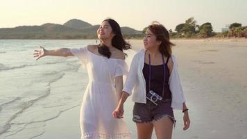 Young Asian lesbian couple walking on beach. Beautiful women friends happy relax walking on beach near sea when sunset in evening. Lifestyle lesbian couple travel on beach concept. photo