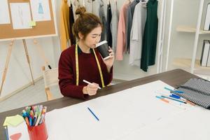 Hermosa diseñadora de moda asiática profesional que trabaja con bocetos de tela y diseño de ropa de dibujo en el estudio. concepto de trabajo de las mujeres de estilo de vida. foto