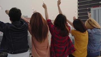 Outdoor shot of young people at rooftop party. Happy group of asian friends enjoy and play sparkler at roof top party at evening sunset. Holiday celebration festive party. Teenage lifestyle party. photo