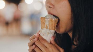 Asian young woman travel in Bangkok, Thailand, beautiful female feeling happy walking and eating ice cream at The Khao San Road. Women travel eat street food in Thailand concept. photo