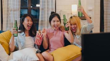 Group of Asian women party at home, female drinking beer watching TV cheer soccer funny moment together on sofa in living room in night. Teenager young friend football fan, celebrate holiday concept. photo