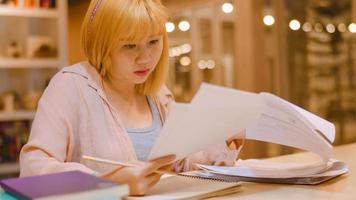 Asian student women reading books in library at university. Young undergraduate girl do homework, read textbook, study hard for knowledge on lecture desk at college campus overtime night. photo
