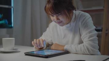 Young asian woman working late using tablet checking social media while relax on desk in night in living room at home. Enjoying time at home concept. photo