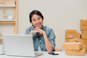 Business woman feeling happy smiling and looking to camera while working in her office at home. Beautiful Asian young entrepreneur owner of SME with small business owner at home office concept. photo