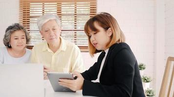 Asia smart female agent offers health insurance for elderly couples by document, tablet and laptop. Aged Asian couple consulting with insurance agent while sitting together with at home. photo