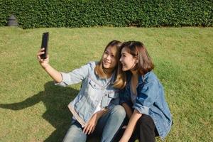 Attractive beautiful asian friends women using a smartphone. Happy young asian teenage at urban city while taking self portraits with her friends together with a smartphone. photo
