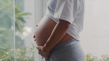Young Asian Pregnant woman holding her belly talking with her child. Mom feeling happy smiling positive and peaceful while take care baby, pregnancy near window in living room at home concept. photo