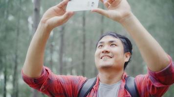 Hiker Asia backpacker man using smartphone for take a picture while on hiking adventure walking in forest, Asian male enjoy his holidays near lots of tree. Lifestyle men travel and relax concept.