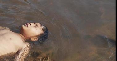 menino está flutuando em uma cachoeira com a luz do sol. ele gosta de brincar com água. video