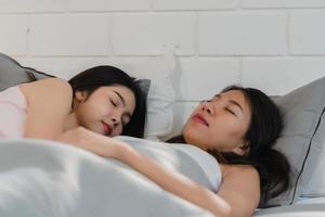 pareja de lesbianas asiáticas duermen juntas en casa. las jóvenes asiáticas lgbtq felices se relajan descansan acostadas en la cama en el dormitorio en casa por la mañana. foto