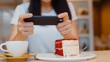 bloguera asiática amigable mujer influyente come pastel en el café de la noche. hermosa jovencita feliz relajarse diversión usando tecnología teléfono móvil tomando una foto de su carga de comida en las redes sociales en el campus universitario.