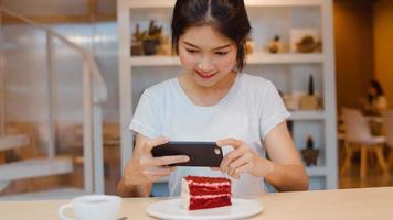 bloguera asiática amigable mujer influyente come pastel en el café de la noche. hermosa jovencita feliz relajarse diversión usando tecnología teléfono móvil tomando una foto de su carga de comida en las redes sociales en el campus universitario.